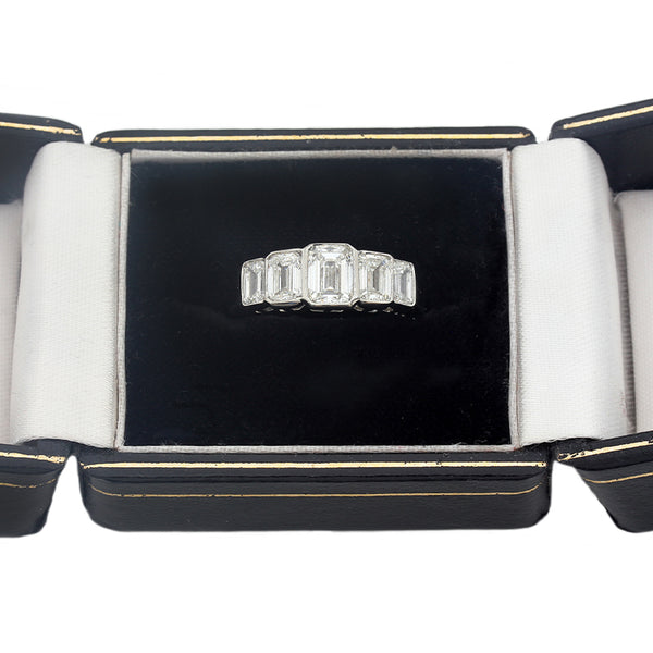 A five stone graduated diamond ring in platinum in a box. Emerald cut Diamonds are rub over set in individual settings