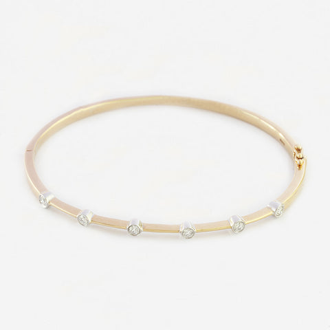 a modern yellow and white gold bangle with 6 round diamonds in a rub over set and oval shaped bangle with hinge