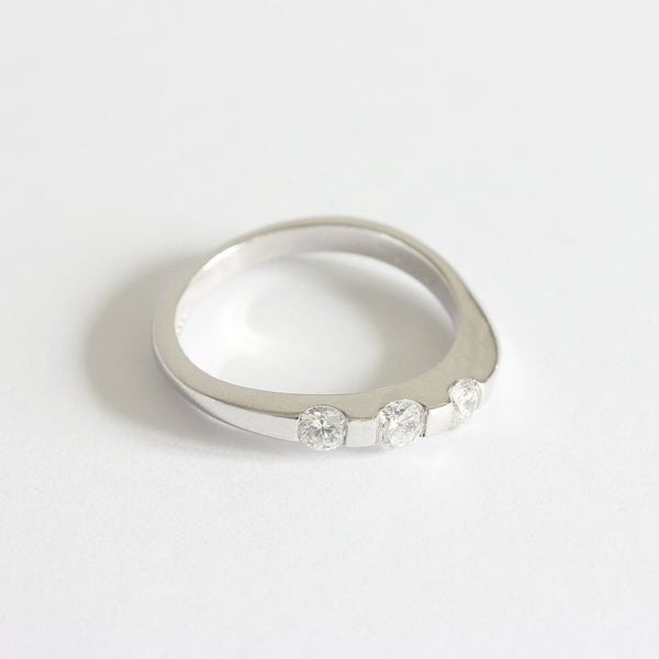 A three stone diamond ring in white gold. The diamonds are set in a tension style with curved shoulders