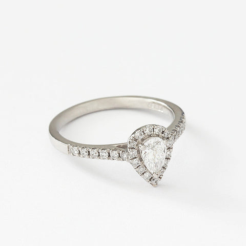 A single pear shaped diamond ring in Platinum. The diamond is in a raised three claw setting with a row of small diamonds around the stone and along each shoulder.