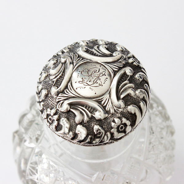 a silver topped perfume bottle with glass base engraving on top with flower pattern dated 1902