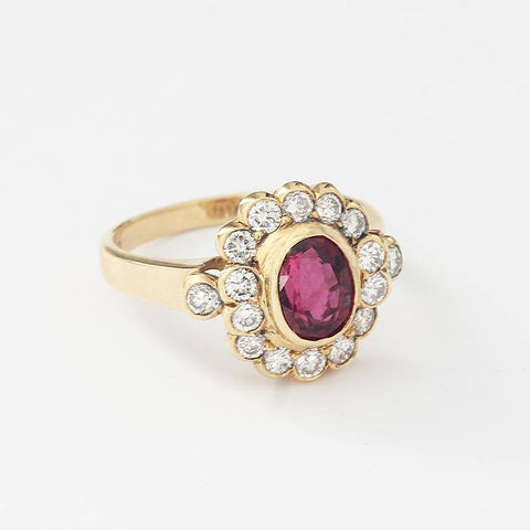 an oval central ruby and a surround of 14 diamonds in a rub-over setting with a yellow gold plain band