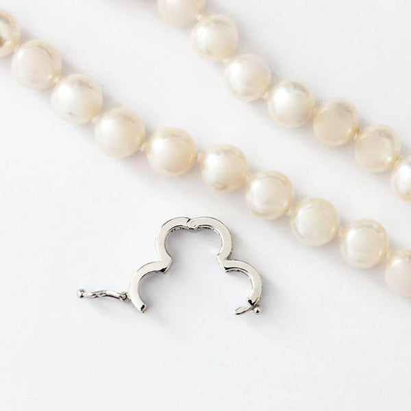 a uniform set of freshwater pearls in a necklace with white gold settings and a white diamond separator attachment and 2 grey pearls at the end