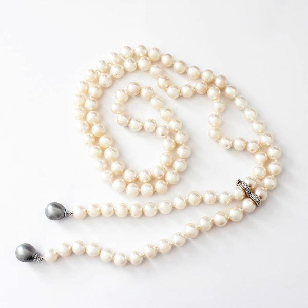 a uniform set of freshwater pearls in a necklace with white gold settings and a white diamond separator attachment and 2 grey pearls at the end