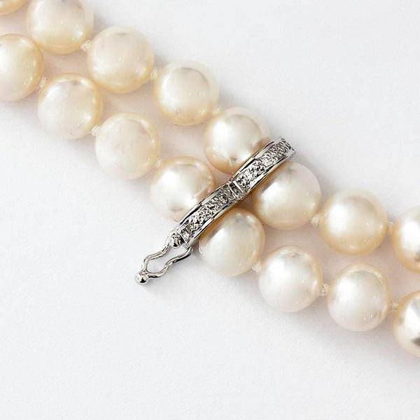 a uniform set of freshwater pearls in a necklace with white gold settings and a white diamond separator attachment and 2 grey pearls at the end